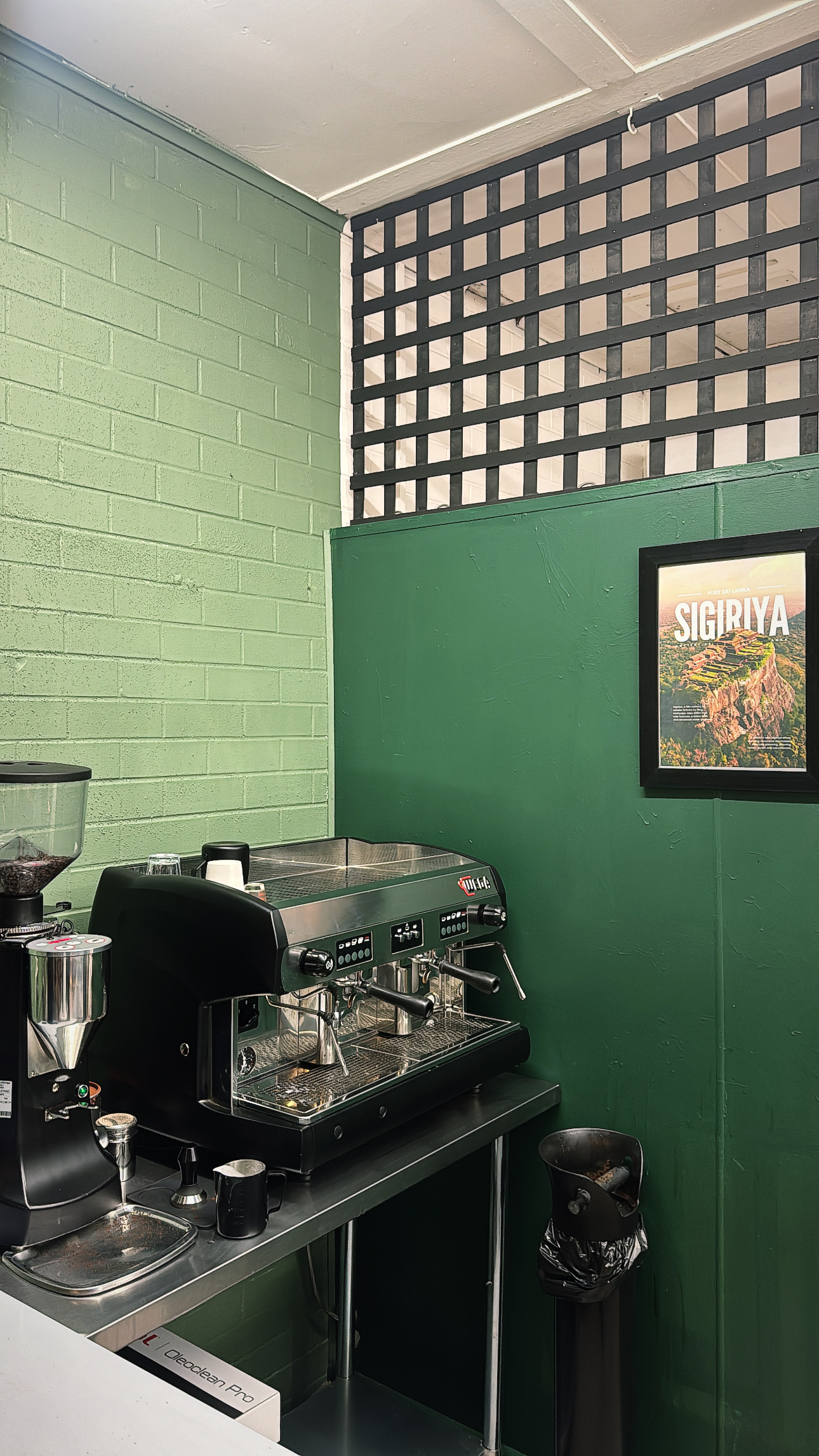 The espresso machine and grinder against the green wall, with a Sigiriya, Sri Lanka travel poster