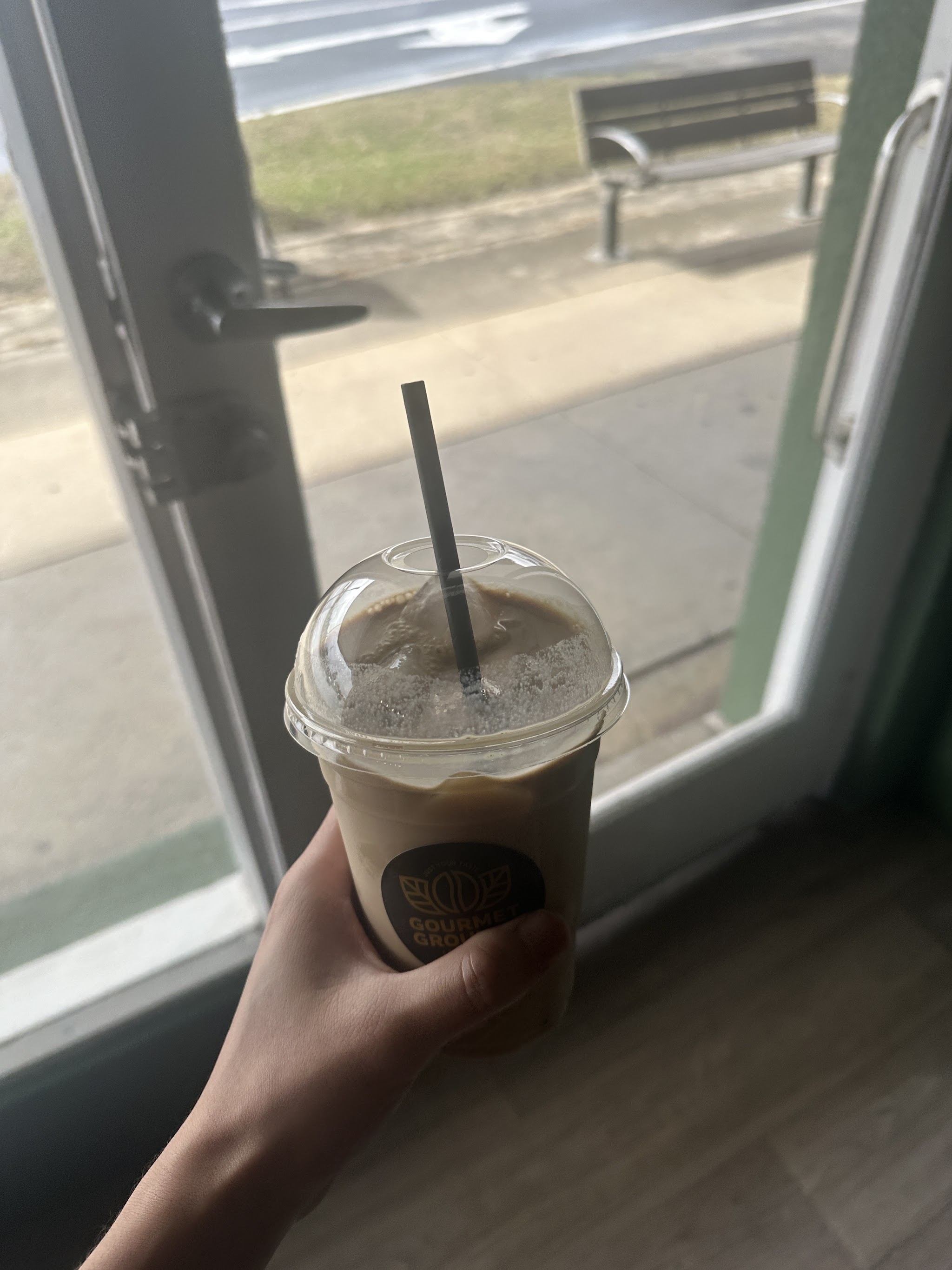 An iced coffee in a Gourmet Grounds cup held up at the shop door